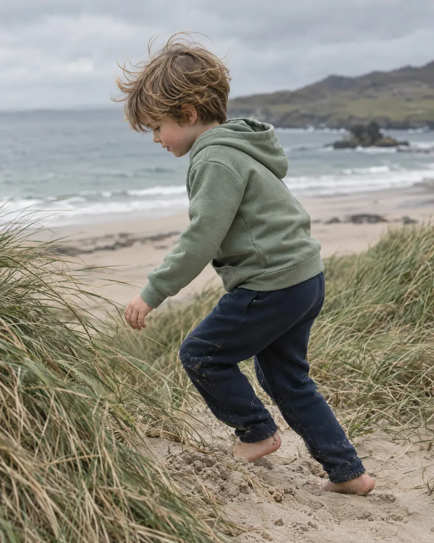 Child in a sage green hoodie playing on a sandy beach